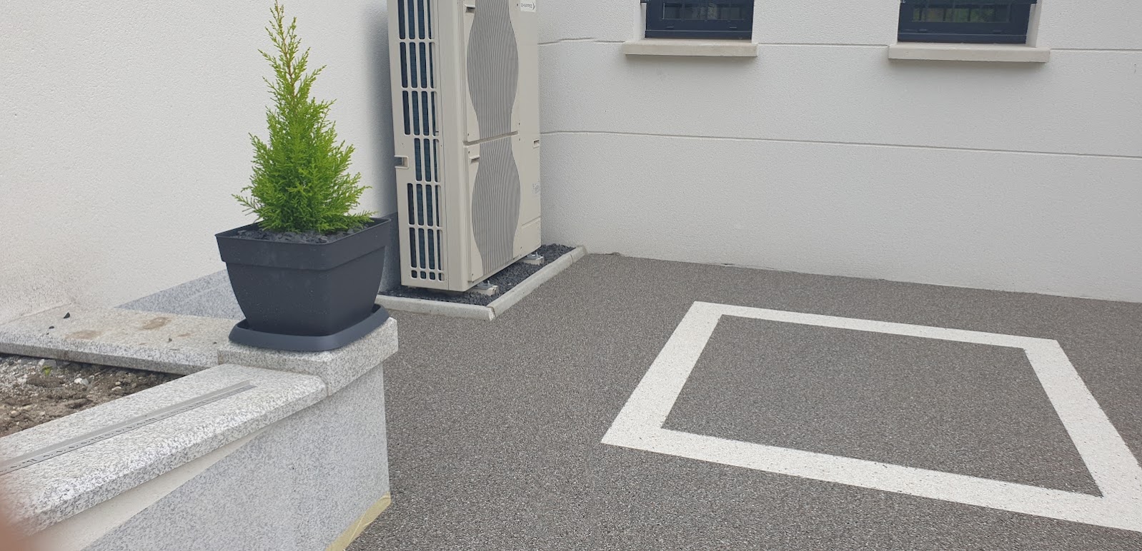 Moquette de pierre bicolore au pied d'une maison, cadre clair sur fond gris